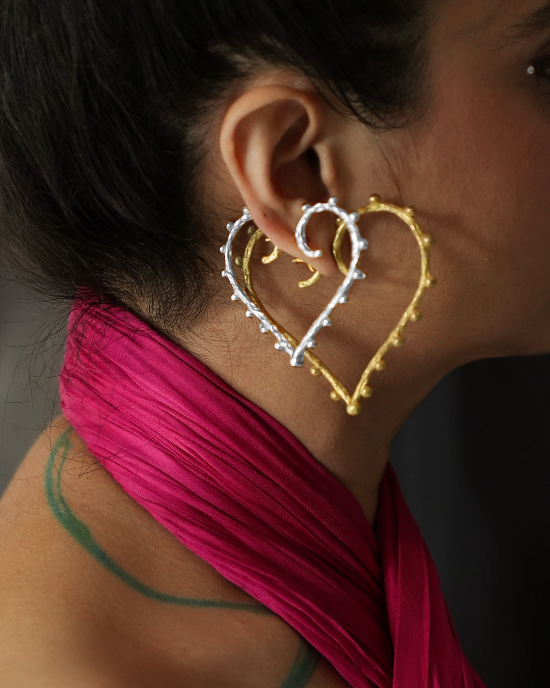 A woman stacking a pair of heart motif earrings in silver and gold.