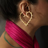 A person showcasing a pair of heart shaped gold earrings.