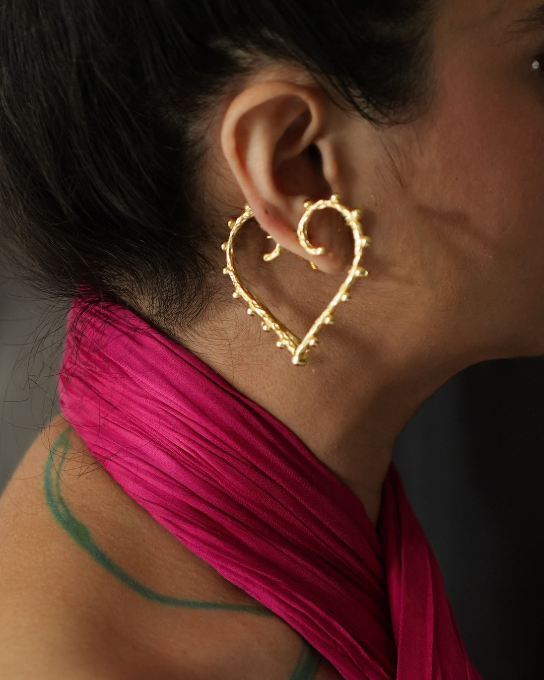 A person showcasing a pair of heart shaped gold earrings.