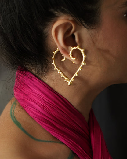 A person showcasing a pair of heart shaped gold earrings.