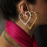 A woman stacking a pair of heart motif earrings in silver and gold.