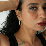 Close-up of a woman with hoop earrings and a tattoo on her neck against a white background