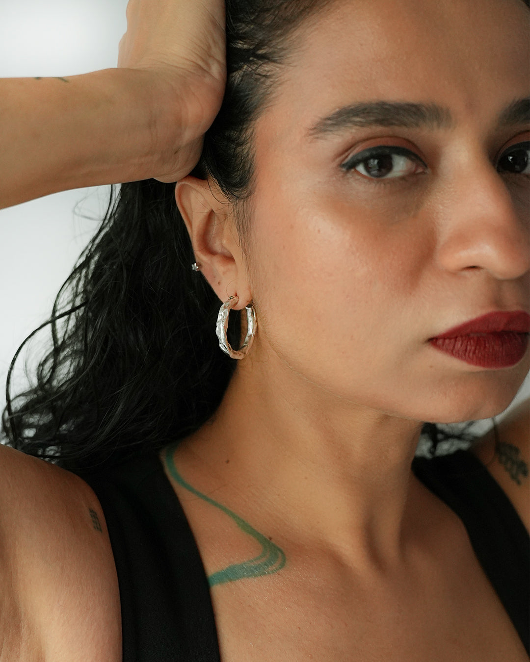 Close-up of a woman with hoop earrings and a tattoo on her neck against a white background