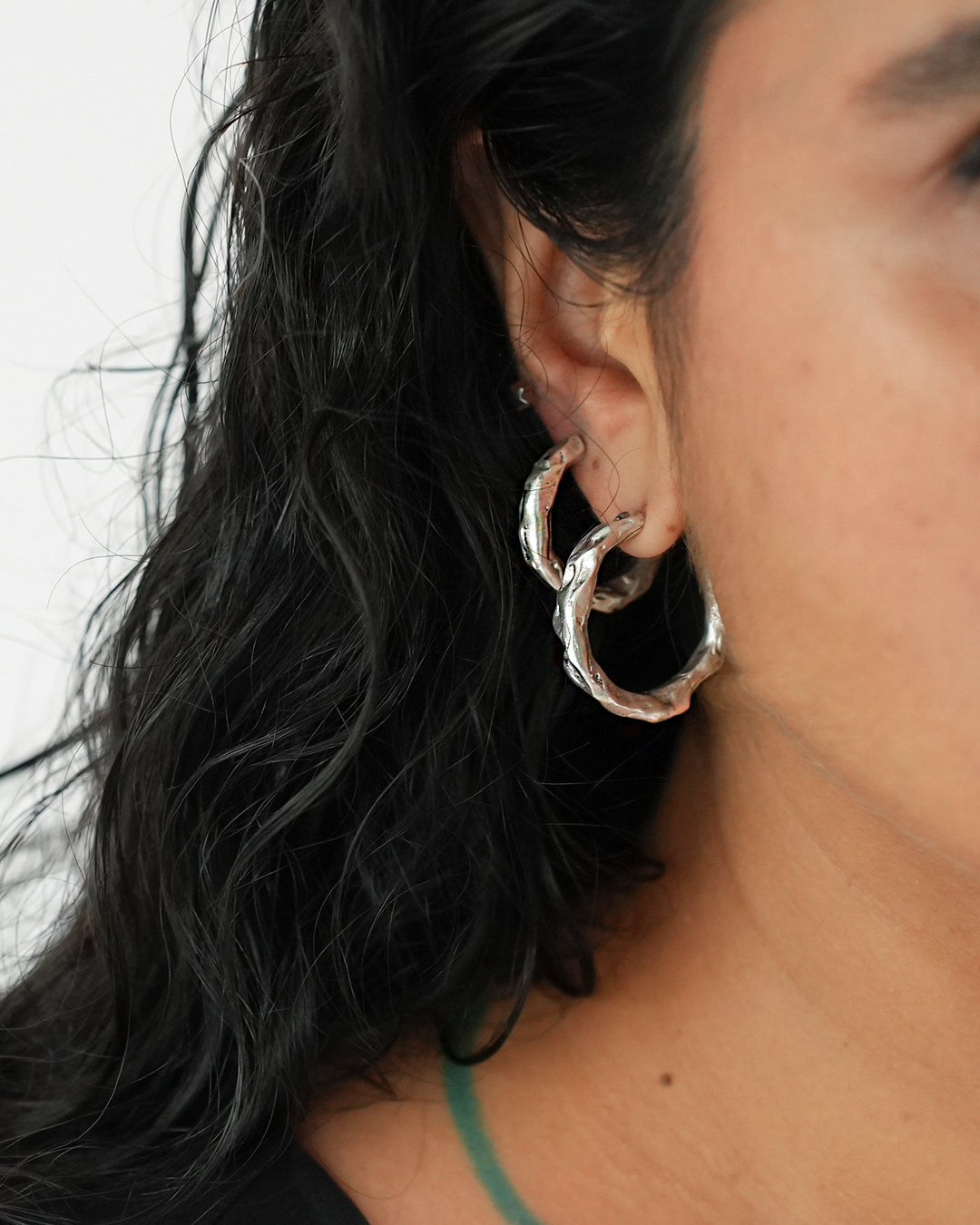 Close-up of a person wearing textured silver hoop earrings
